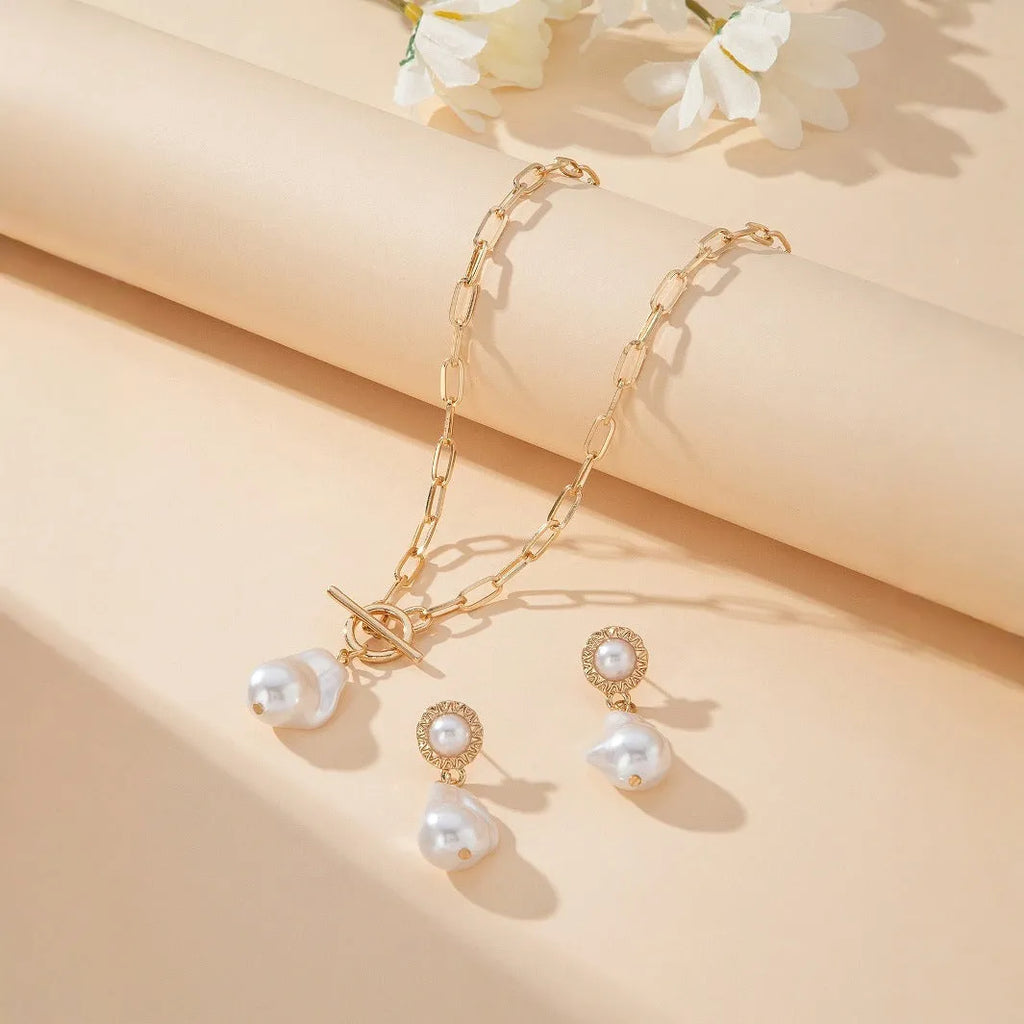 Gold retro baroque style necklace and earring set with pearl details on a white background.