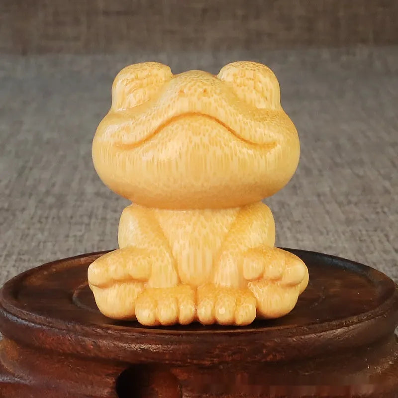 Solid bamboo smiling frog carving ornament with cartoon style on a wooden surface.