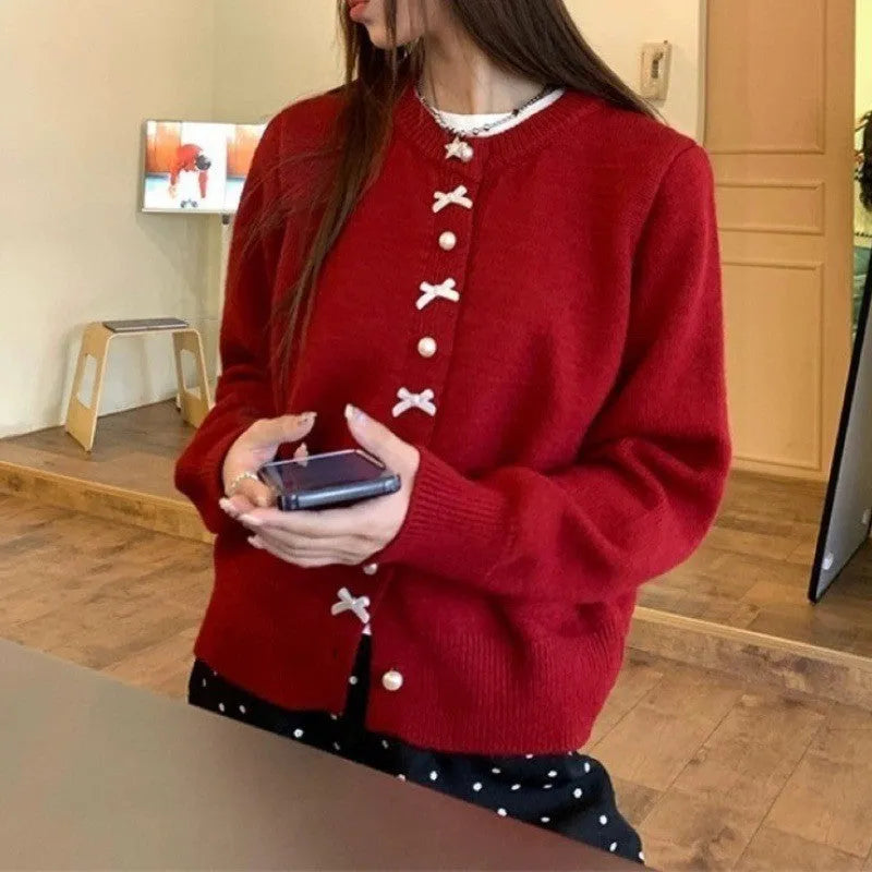 Women's cardigan sweater with a decorative bow and pearl buttons, shown in a solid colour.
