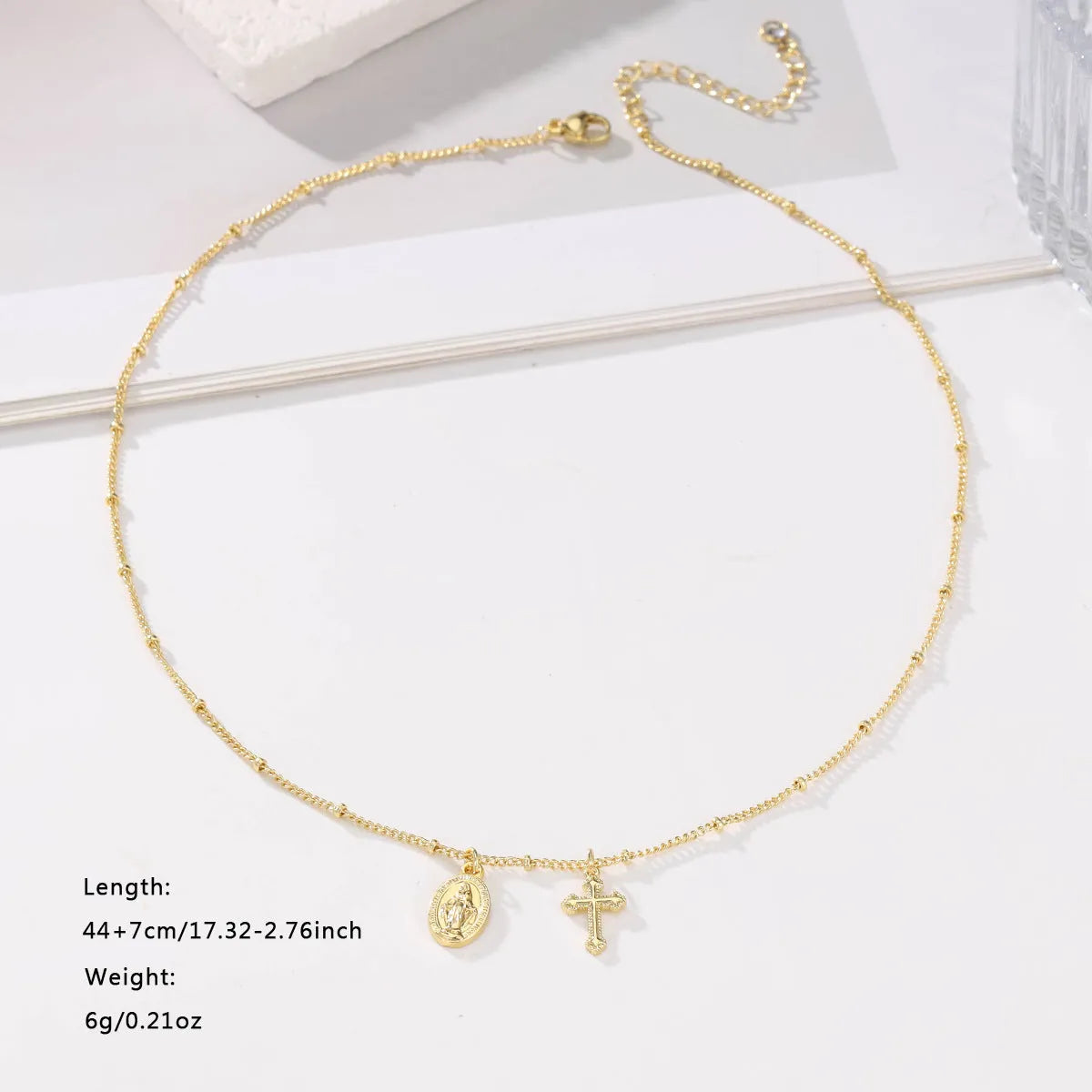 Gold-coloured Virgin Mary and cross pendant necklace on a chain.