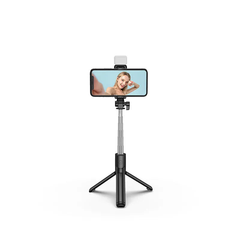 Black Bluetooth selfie stick with extended tripod legs and a fill light, holding an iPhone.