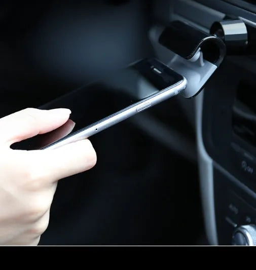 Black gravity car phone holder with 360-degree rotating bracket mounted on a car dashboard holding a mobile phone.