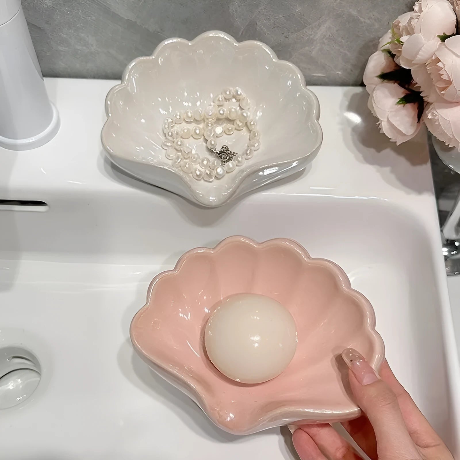 White plastic shell-shaped soap dish with a raised centre, placed on a bathroom counter.
