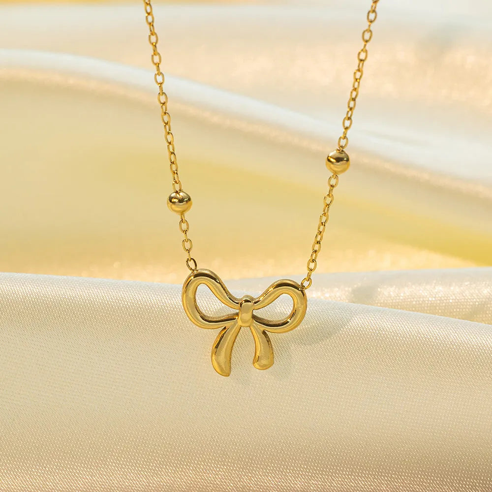 Gold-coloured titanium steel bow necklace with cross chain detail on white background