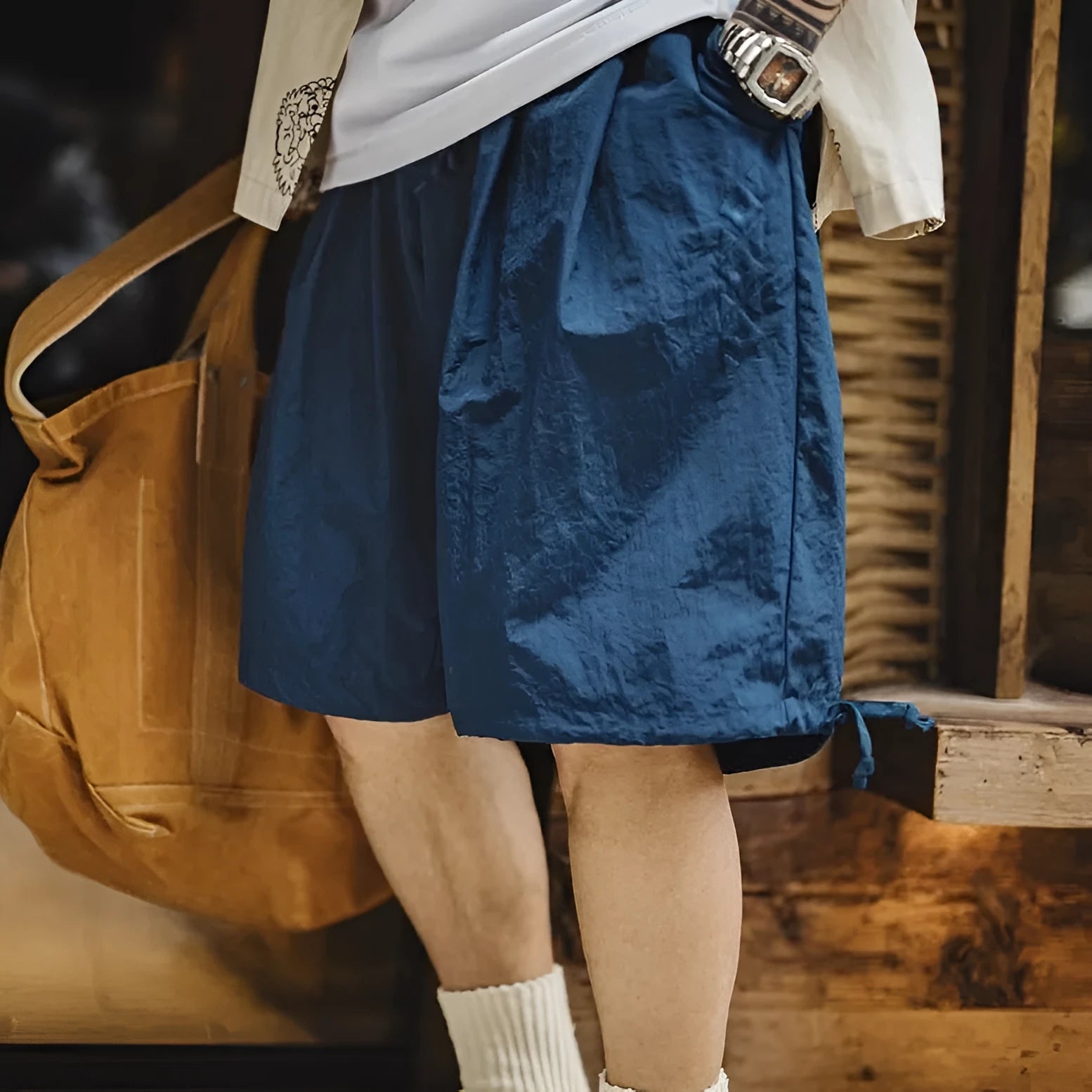 Men's loose Prussian Blue nylon shorts with embroidery on a beach background.