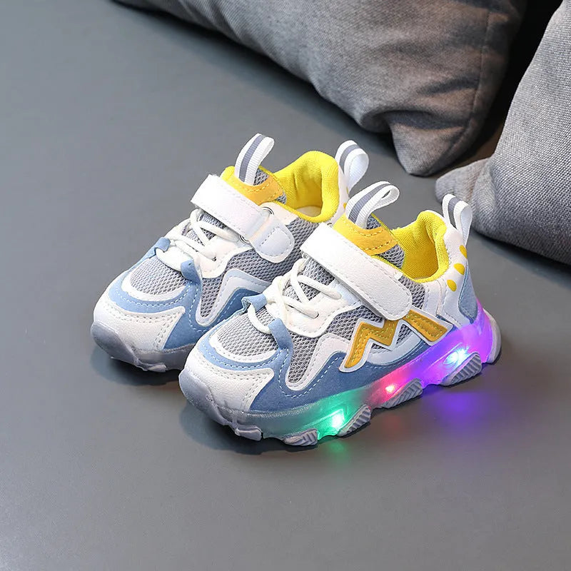 Children's black sneakers with mesh panels, Velcro strap, and rubber sole on a grey background.