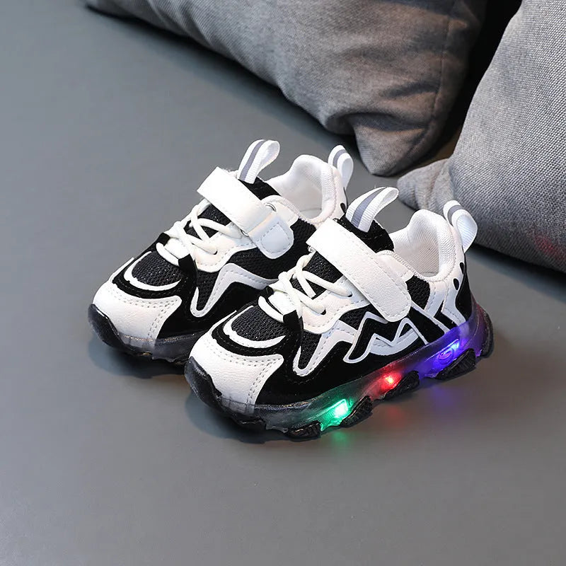 Children's black sneakers with mesh panels, Velcro strap, and rubber sole on a grey background.