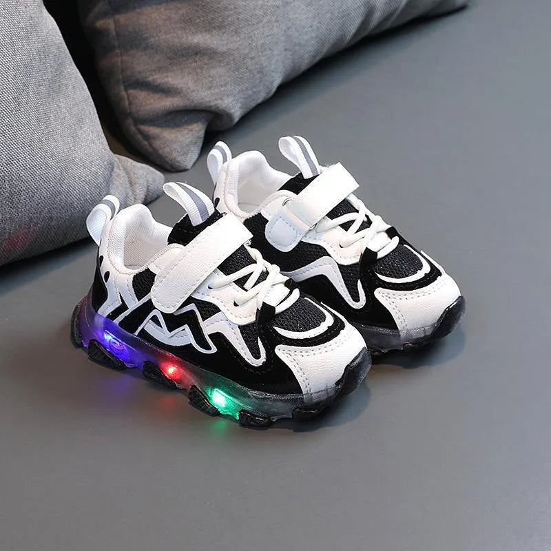 Children's black sneakers with mesh panels, Velcro strap, and rubber sole on a grey background.
