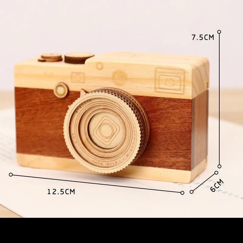 Pine wood music box with rotating camera figurine on top, shown next to its mini carton packaging.