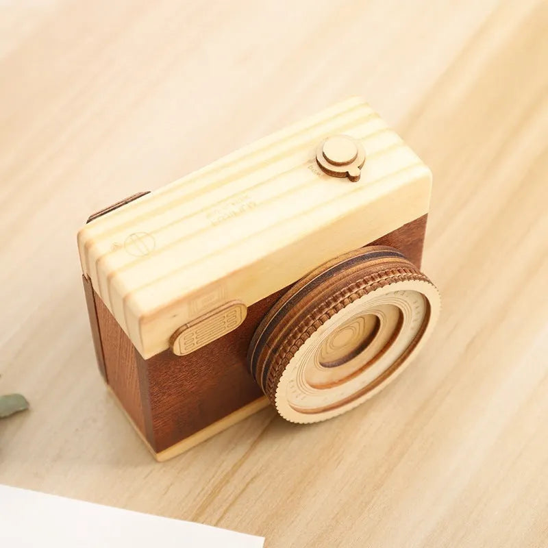 Pine wood music box with rotating camera figurine on top, shown next to its mini carton packaging.