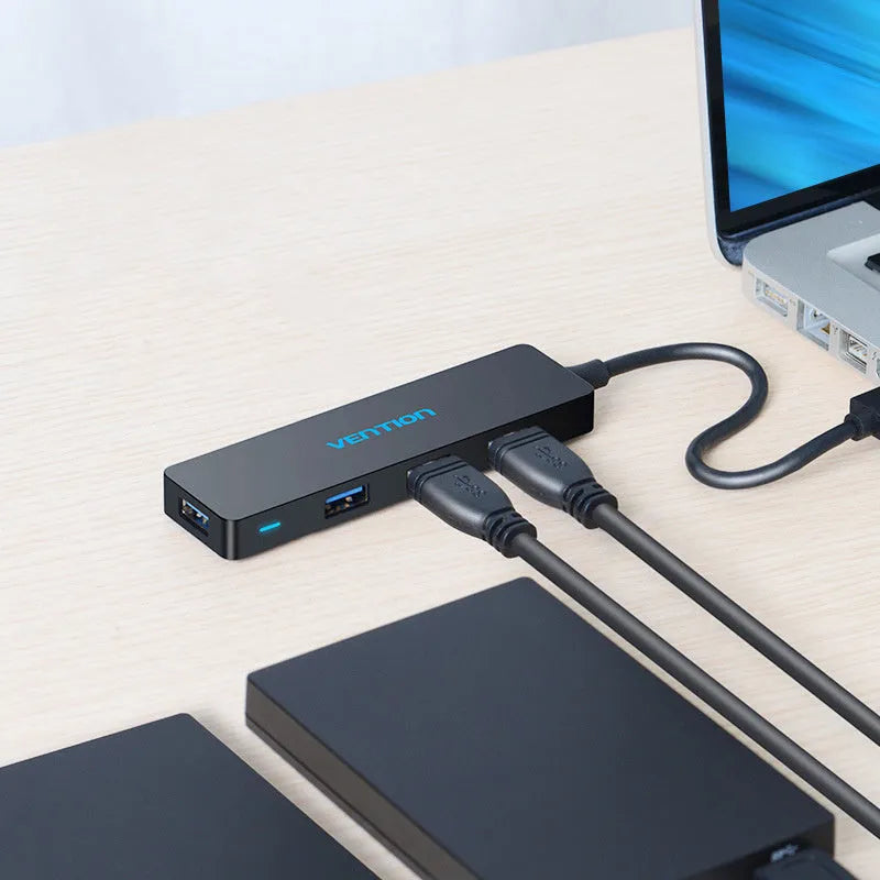 Black four-port USB 3.0 hub with a short cable and nickel-plated connectors on a desk.