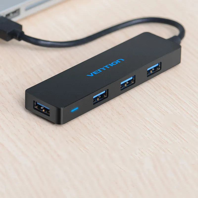 Black four-port USB 3.0 hub with a short cable and nickel-plated connectors on a desk.