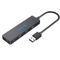 Black four-port USB 3.0 hub with a short cable and nickel-plated connectors on a desk.