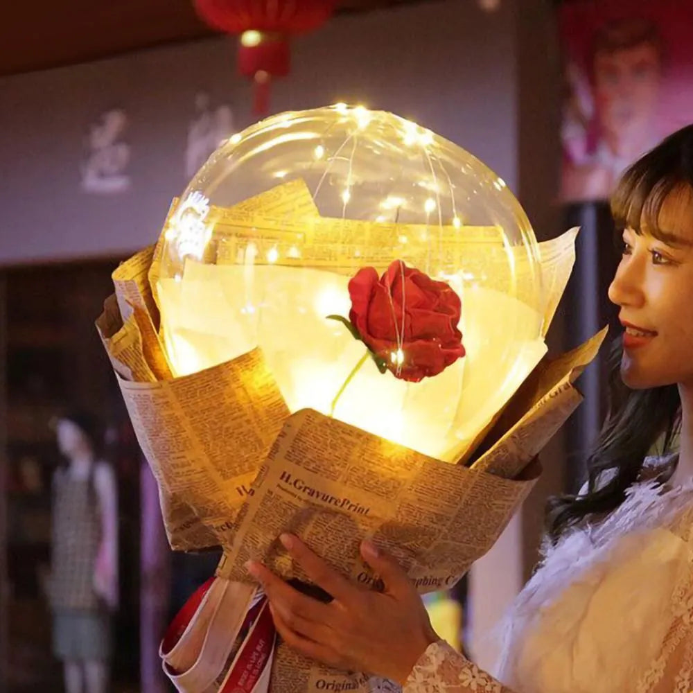Transparent LED balloon rose bouquet with pink artificial flower and glowing light on dark background
