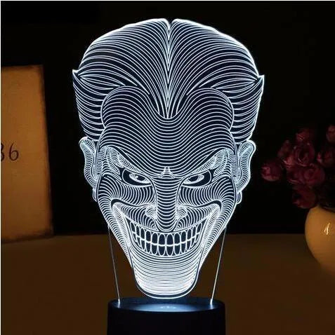 A 3D acrylic LED table lamp with a remote control on a desk, showing its colourful gradient light mode.