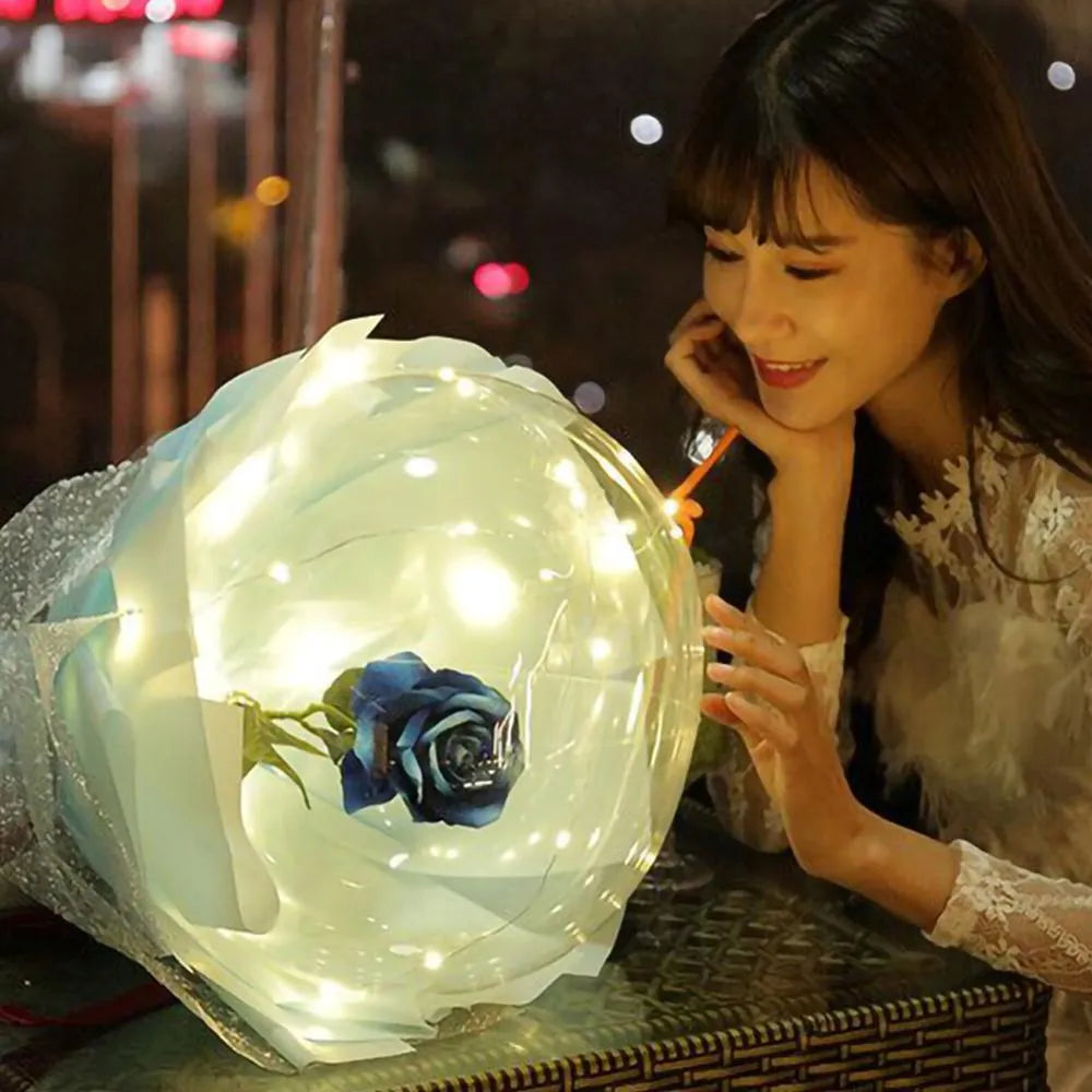 Transparent LED balloon rose bouquet with pink artificial flower and glowing light on dark background