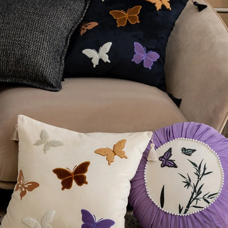 Square decorative cushion with embroidered butterfly pattern in beige, black, or purple colours.