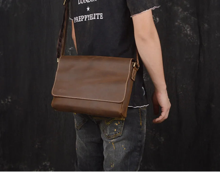 Vintage brown leather mens messenger bag with a shoulder strap, shown open to reveal internal organiser pockets.