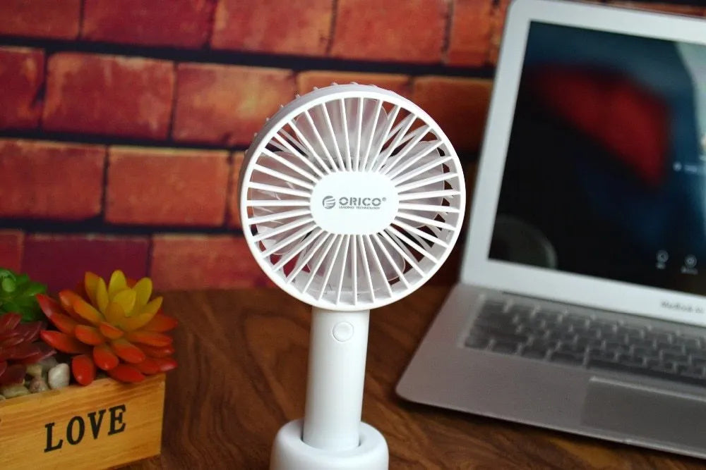 White ORICO FH1 handheld USB rechargeable small fan with three-speed buttons on a desktop.