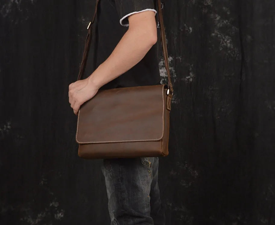Vintage brown leather mens messenger bag with a shoulder strap, shown open to reveal internal organiser pockets.