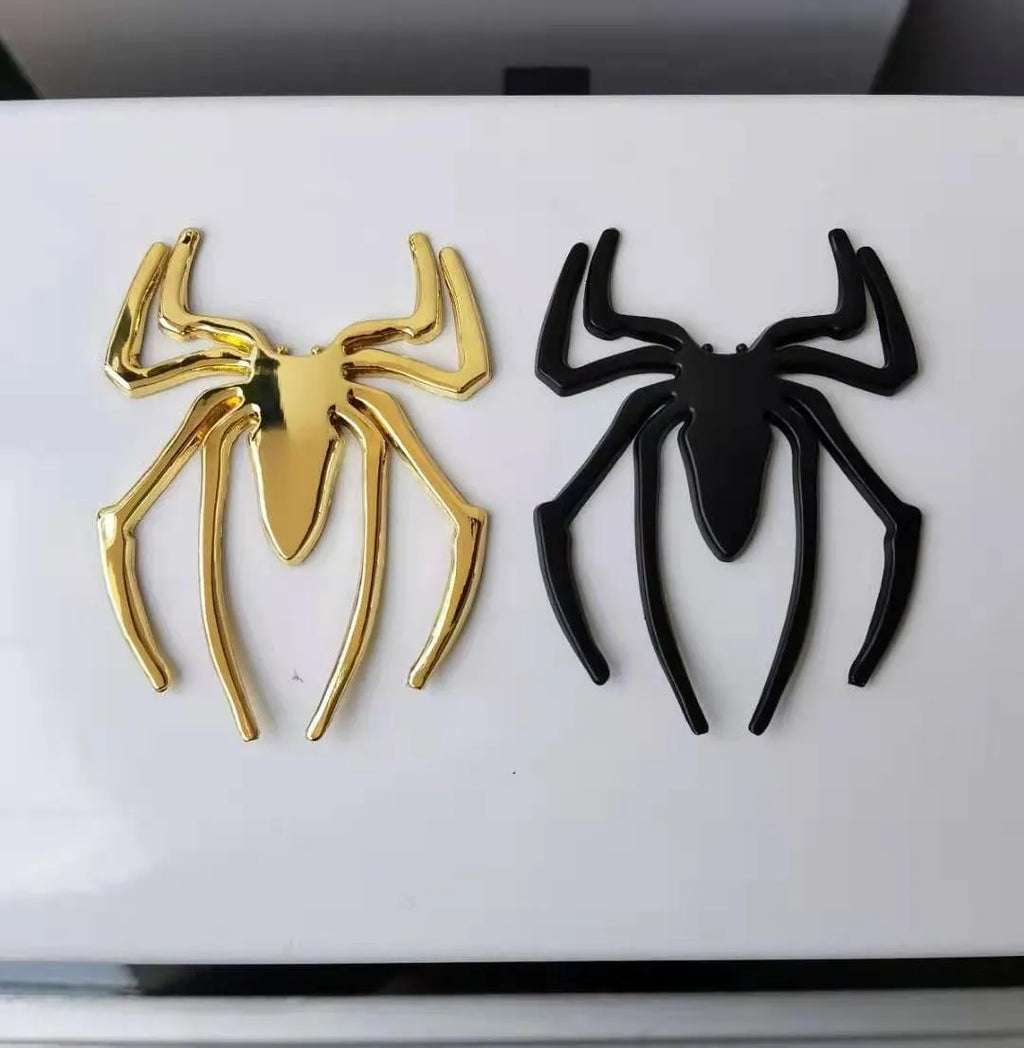 Three-dimensional metal spider bumper sticker in metallic finish on a car bumper.