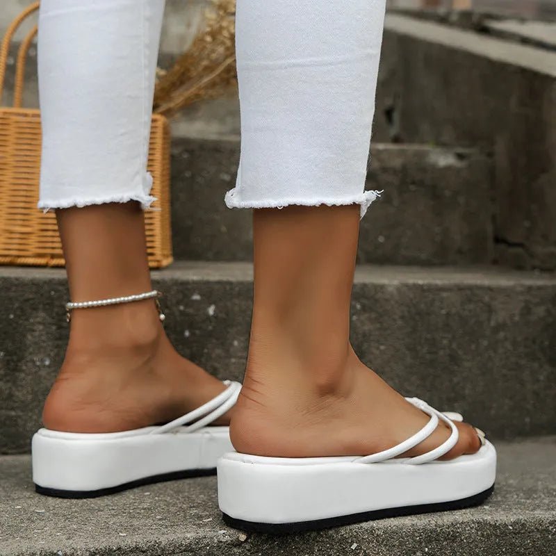 White flip-flops with thick rubber sole and herringbone pattern strap on beach background