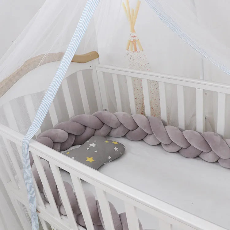 Braided knot crib bumper in spandex velvet wrapped around a white cot for infant safety protection.