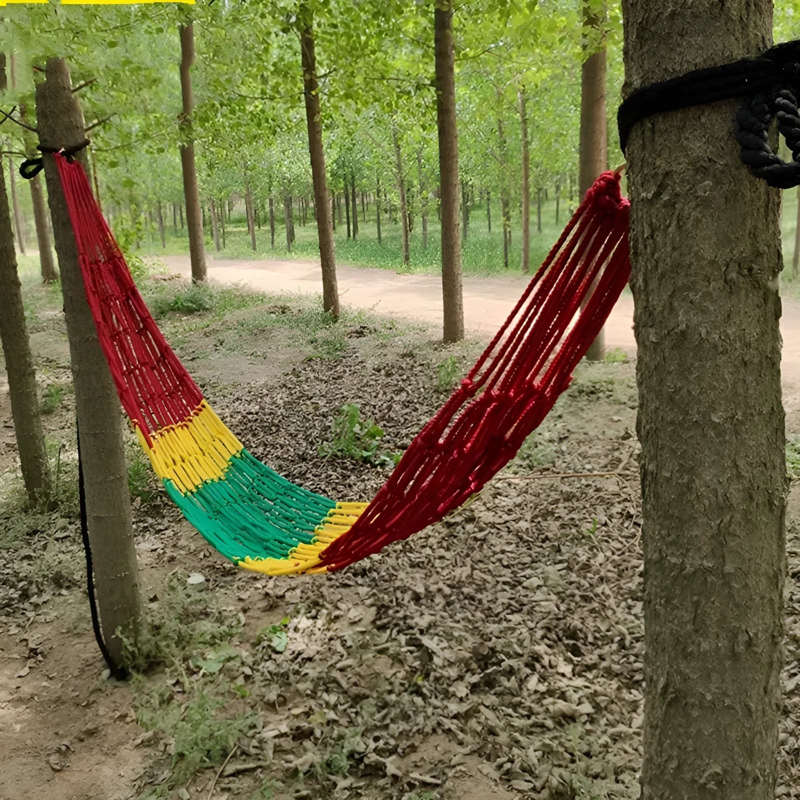 Nylon rope mesh outdoor hammock hung between two trees, showing its open weave and included tying ropes.