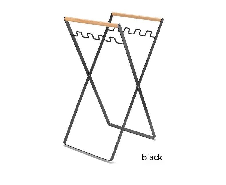 Black folding iron trash rack with a wooden handle holding a rubbish bag outdoors.