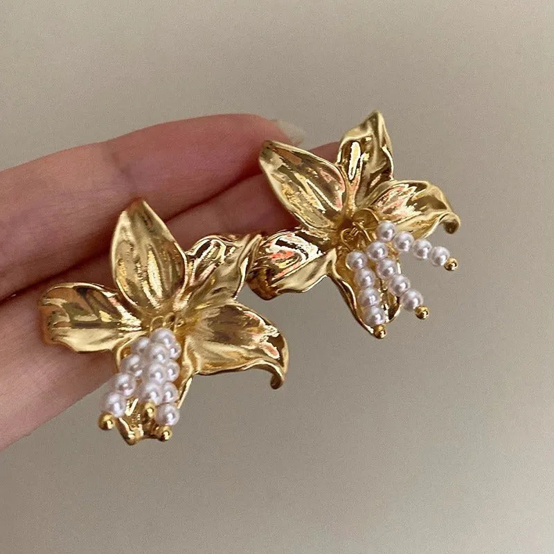 Gold pearl flower earrings with metal post back on white background, exaggerated floral shape