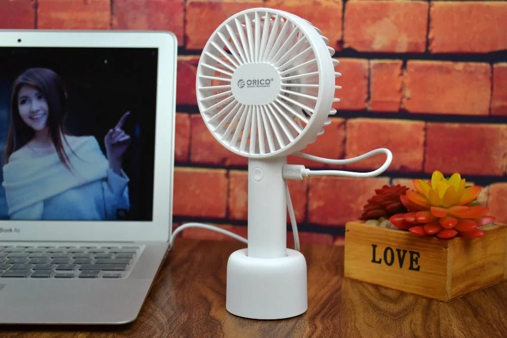White ORICO FH1 handheld USB rechargeable small fan with three-speed buttons on a desktop.