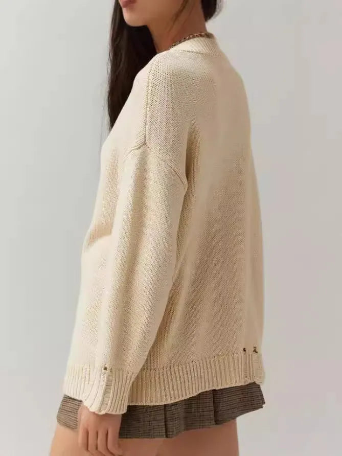Women's loose-fitting beige jacquard knit sweater on a hanger, showing round neck and long sleeves.