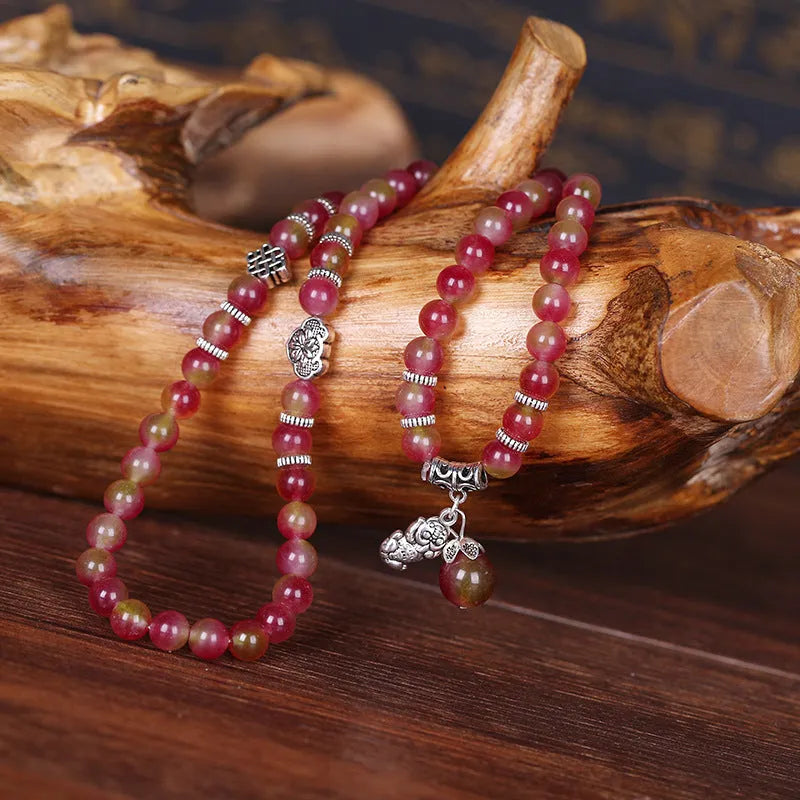 Close-up of a handmade watermelon crystal bracelet with a central Chinese knot and geometric beads.