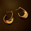 Close-up of gold twisted geometric metal earrings with a round design element.