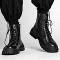 Men's black mid-top leather lace-up boots with a rubber sole on a wooden floor