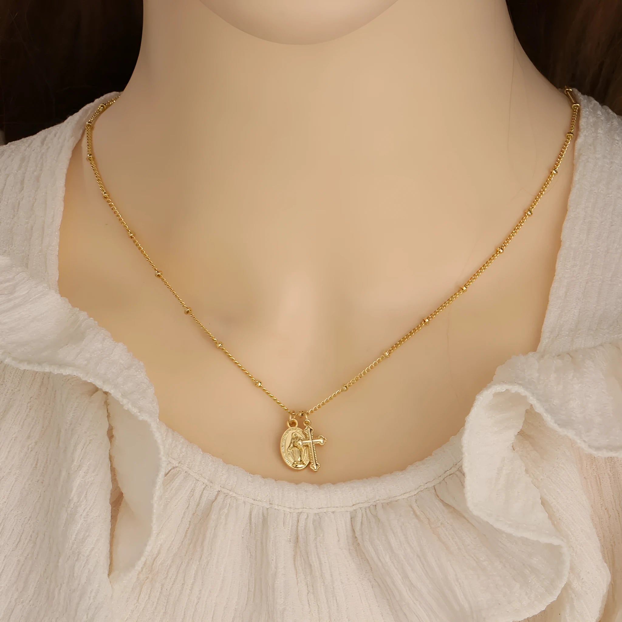 Gold-coloured Virgin Mary and cross pendant necklace on a chain.