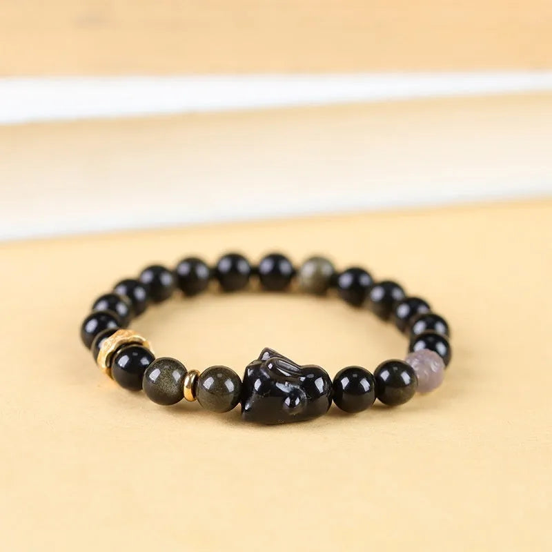 Handmade unisex lying rabbit Jin Yaoshi obsidian bracelet with gray agate and brass beads on neutral background
