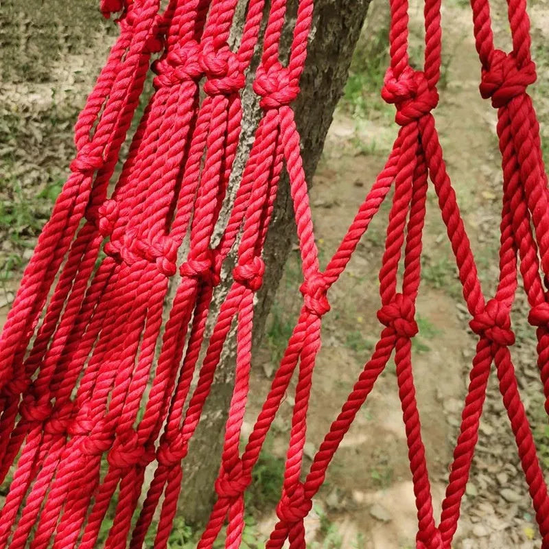 Nylon rope mesh outdoor hammock hung between two trees, showing its open weave and included tying ropes.