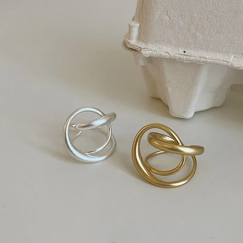 Geometric open ring for women with three-dimensional interlaced matte metal design in gold or silver.