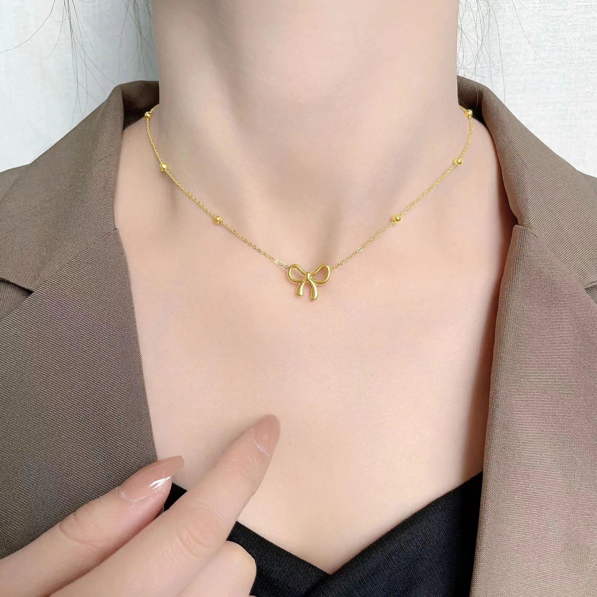 Gold-coloured titanium steel bow necklace with cross chain detail on white background