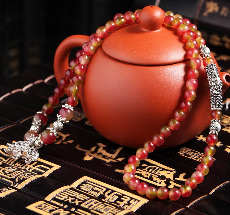Close-up of a handmade watermelon crystal bracelet with a central Chinese knot and geometric beads.