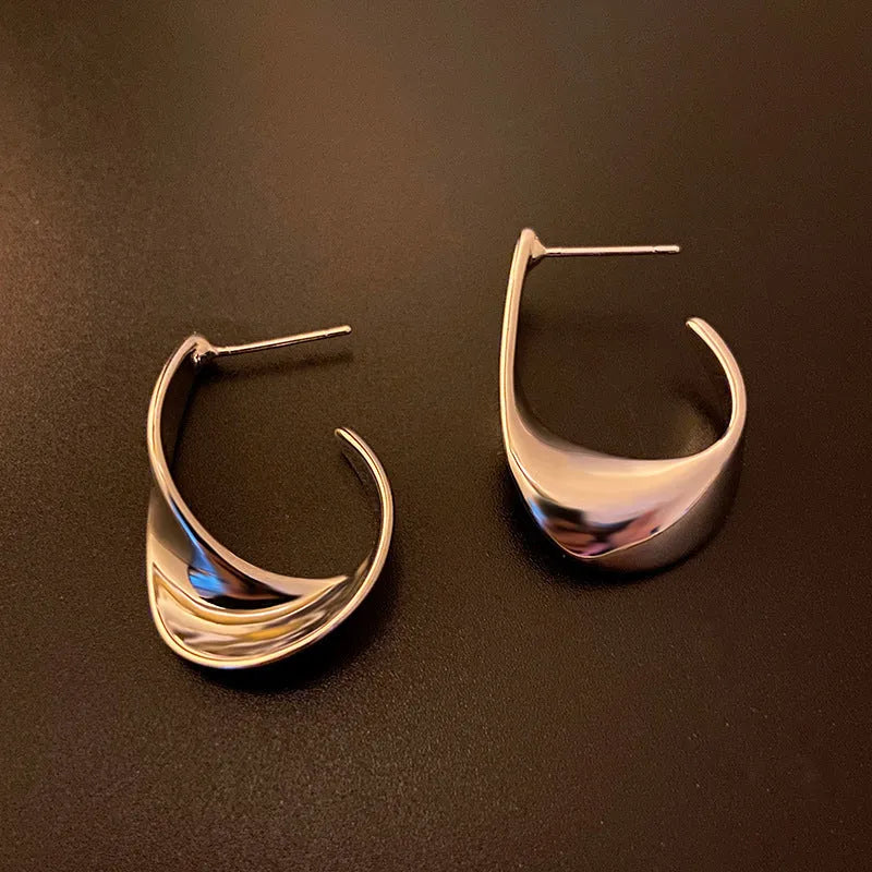 Close-up of gold twisted geometric metal earrings with a round design element.