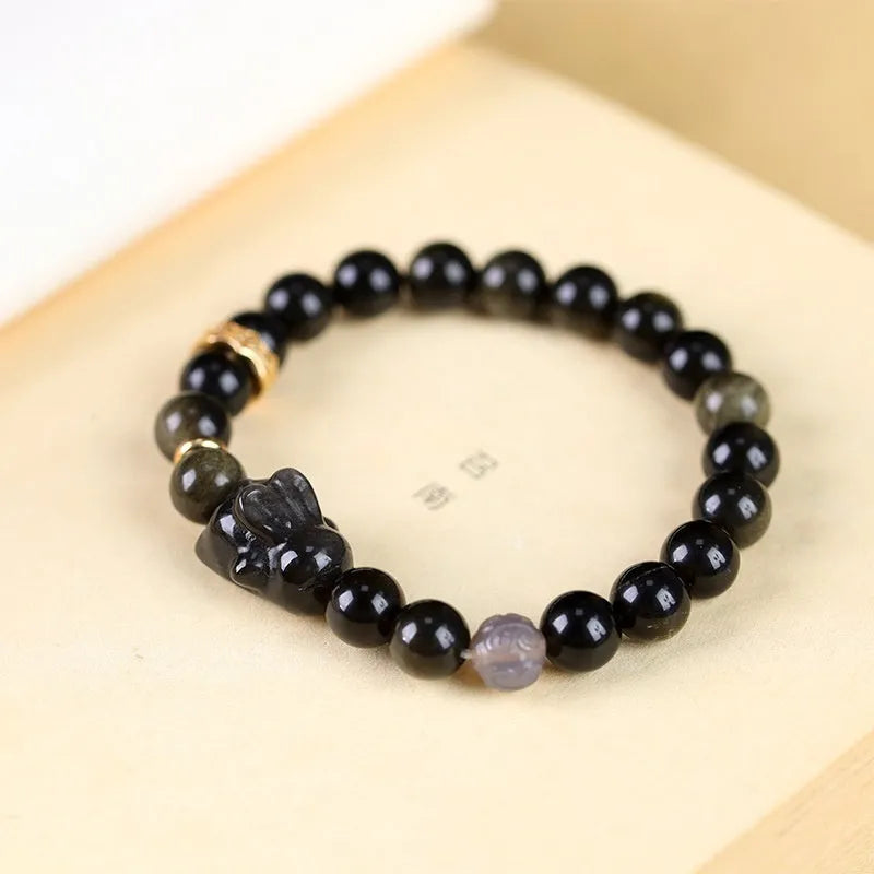 Handmade unisex lying rabbit Jin Yaoshi obsidian bracelet with gray agate and brass beads on neutral background