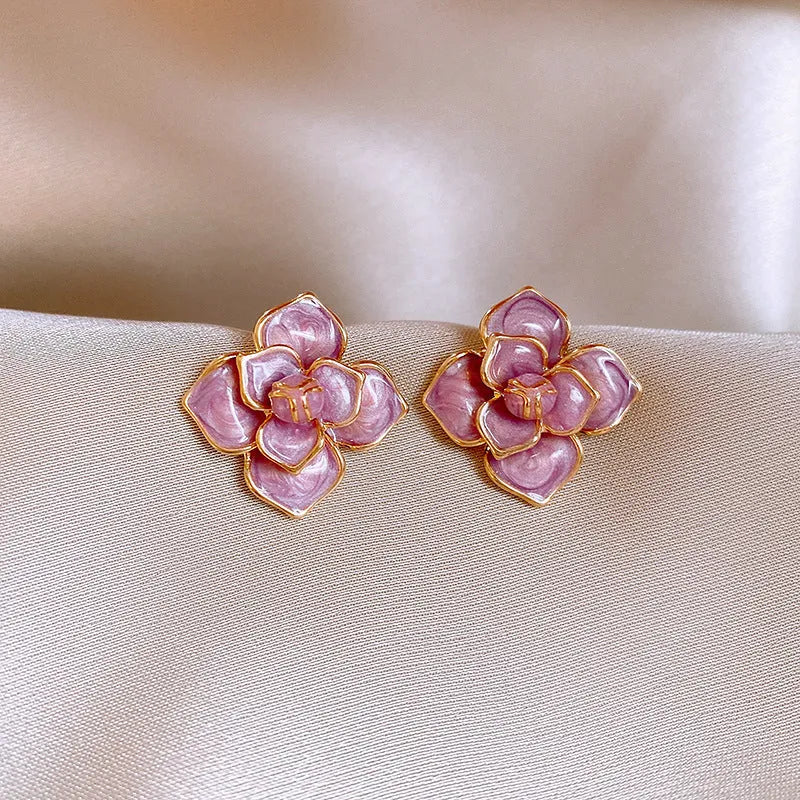 A pair of purple and gold floral stud earrings with detailed needlework and an oil-spot glaze finish.