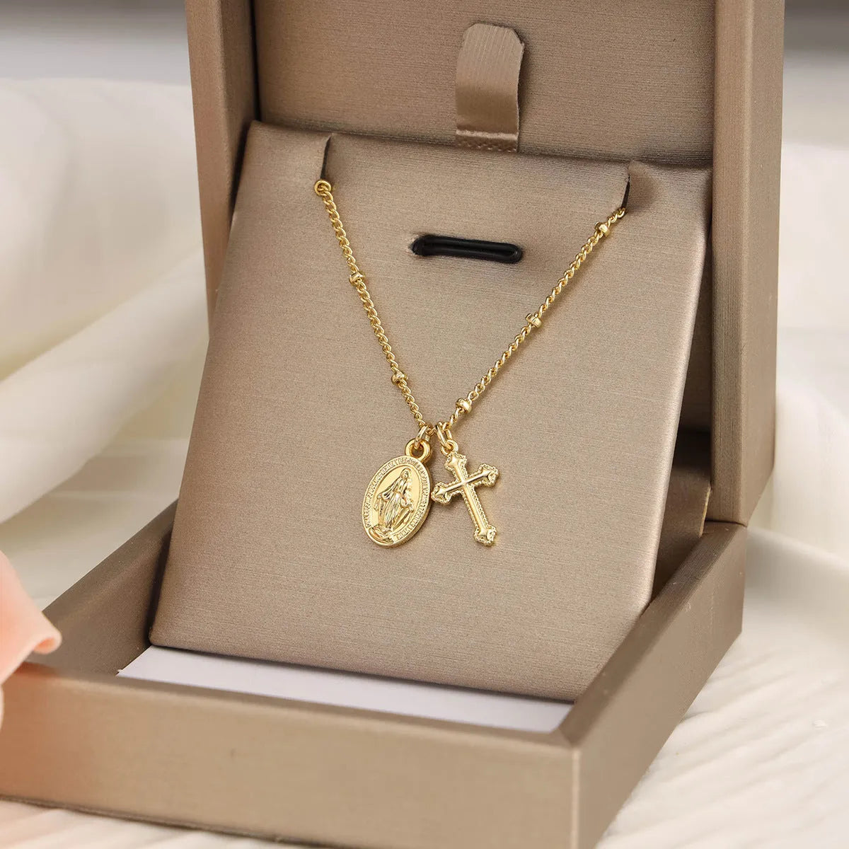 Gold-coloured Virgin Mary and cross pendant necklace on a chain.