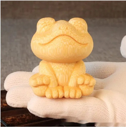 Solid bamboo smiling frog carving ornament with cartoon style on a wooden surface.