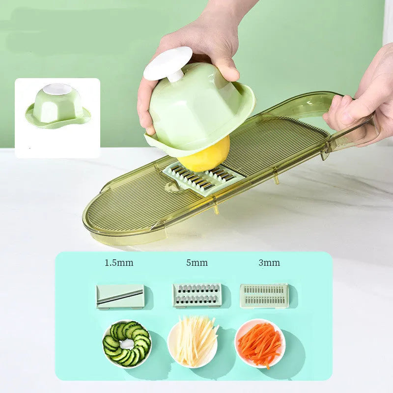 Transparent green vegetable chopper with multiple stainless steel blades and a hand protector on a kitchen worktop