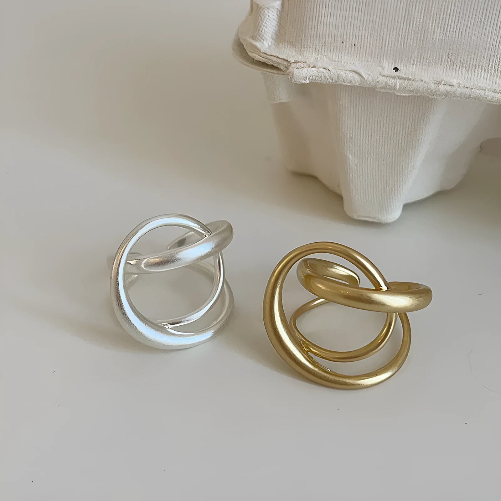 Geometric open ring for women with three-dimensional interlaced matte metal design in gold or silver.