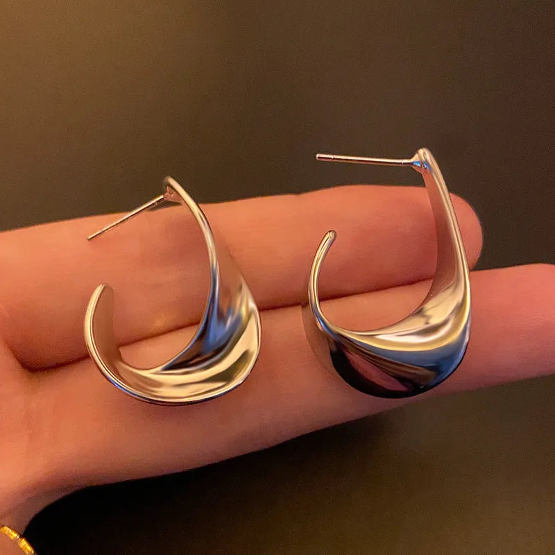 Close-up of gold twisted geometric metal earrings with a round design element.