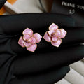 A pair of purple and gold floral stud earrings with detailed needlework and an oil-spot glaze finish.